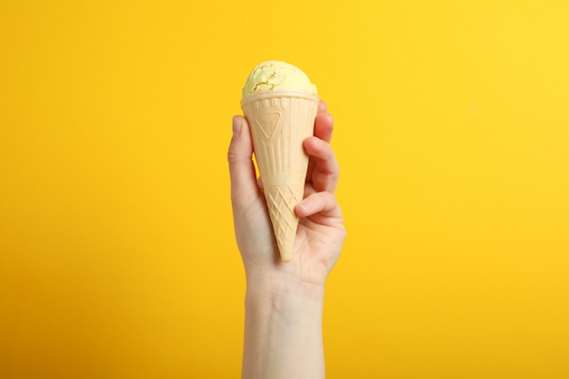 Female hand holds ice cream on yellow surface