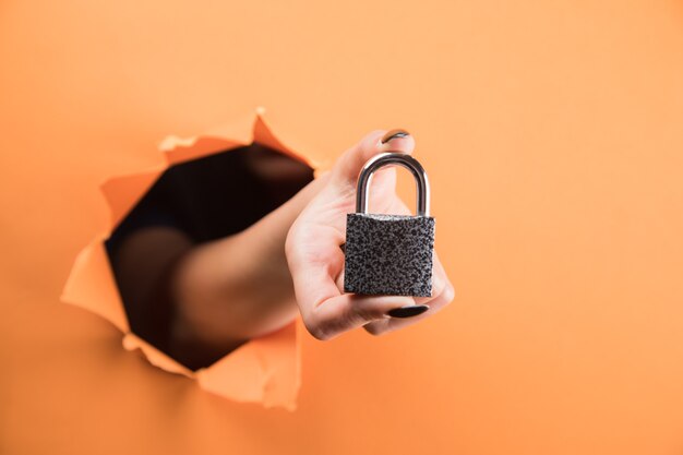 Female hand holds lock on orange background