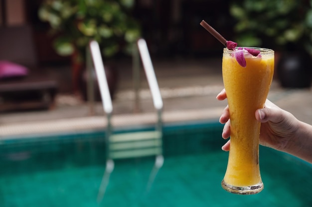 Female hand holds mango smoothie in a high glass