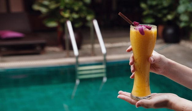 Female hand holds mango smoothie in a high glass