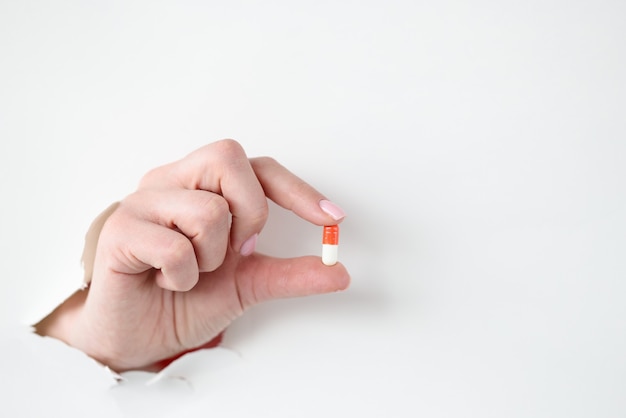 Female hand holds medical pill through hole through white paper