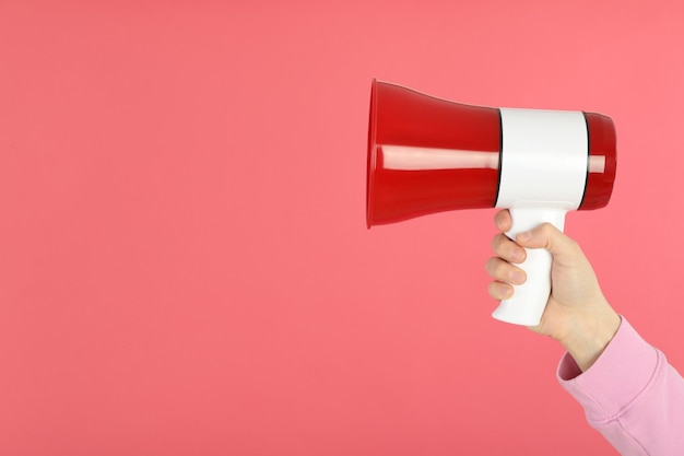 Female hand holds megaphone on pink background