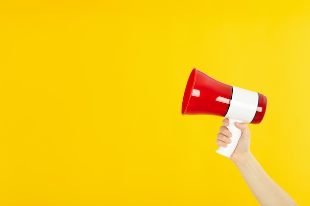 Female hand holds megaphone on yellow background