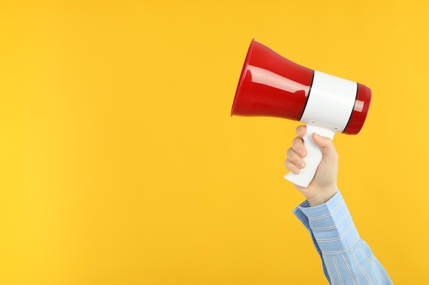 Female hand holds megaphone on yellow background