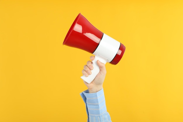 Female hand holds megaphone on yellow background