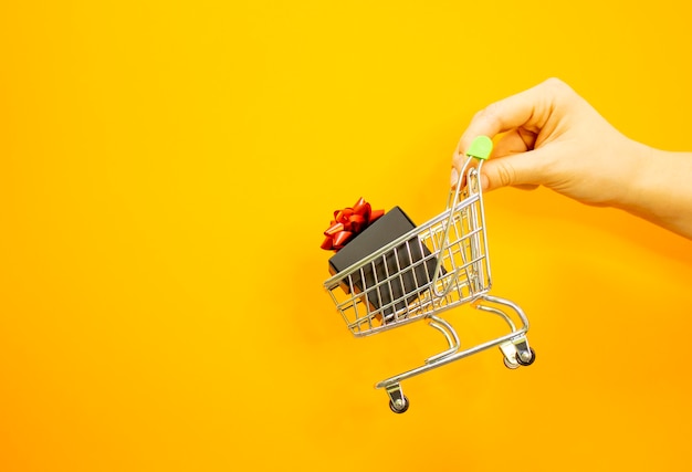 A female hand holds a metal trolley with a box on a yellow background with empty space for text