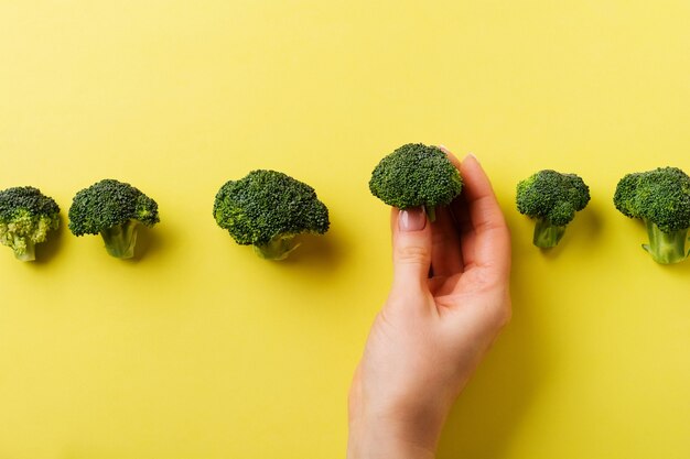 La mano femminile tiene un broccolo verde fresco sdraiato su sfondo giallo chiaro. vista dall'alto.