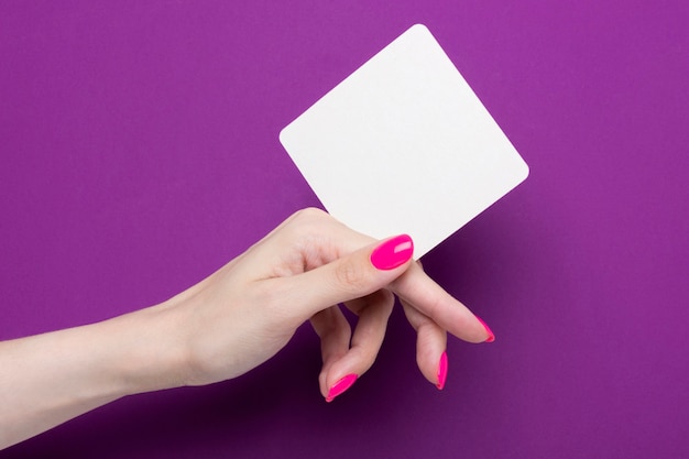 Female hand holds a one square coaster on a purple background.