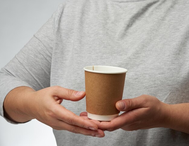 Photo female hand holds paper brown disposable cup for coffee and tea part of body on a white background