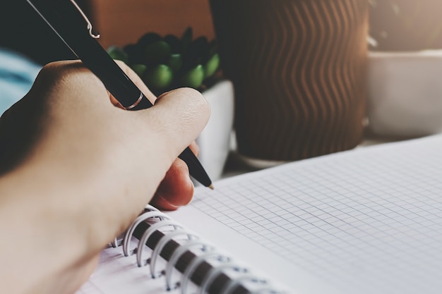 Female hand holds a pen and writes in a notebook