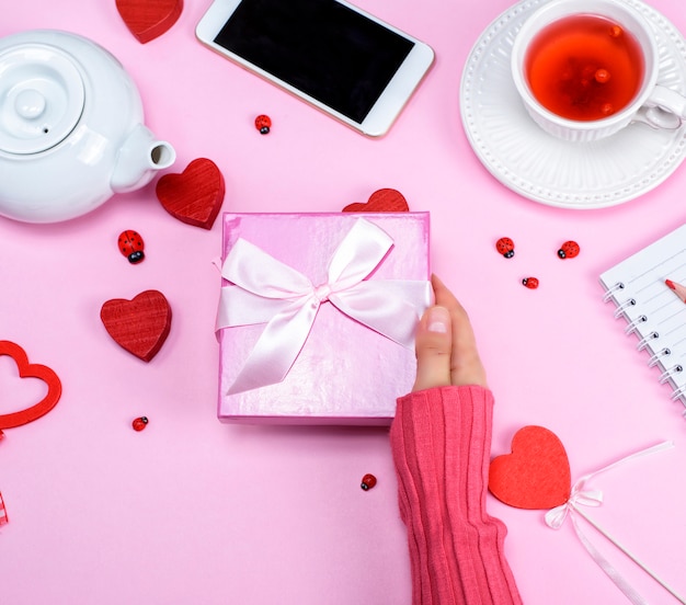 A female hand holds a pink box with a bow over the table 