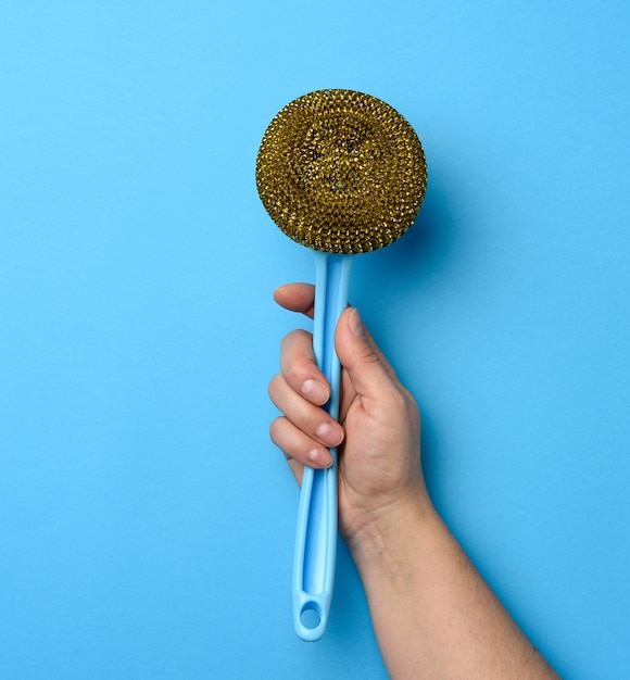 Female hand holds plastic brush with a handle on blue