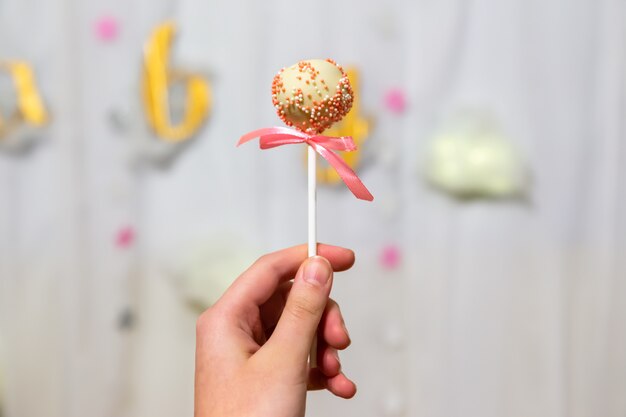 Photo female hand holds pop cakes on pastel background. white chocolate cake pop decorated with colorfull confectionery sprinkles. party concept.