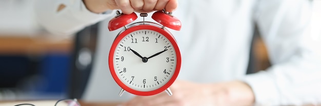 Female hand holds red alarm clock at working table. Time management and deadlines concept