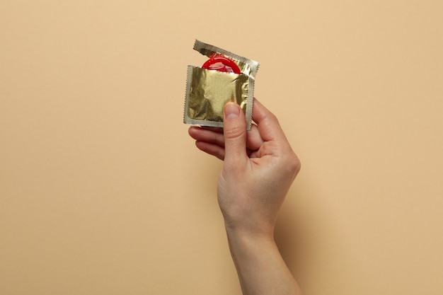 Female hand holds red condom on beige surface