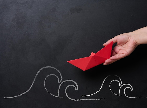 A female hand holds a red paper boat with chalkdrawn waves below representing the concept of mentorship and business support