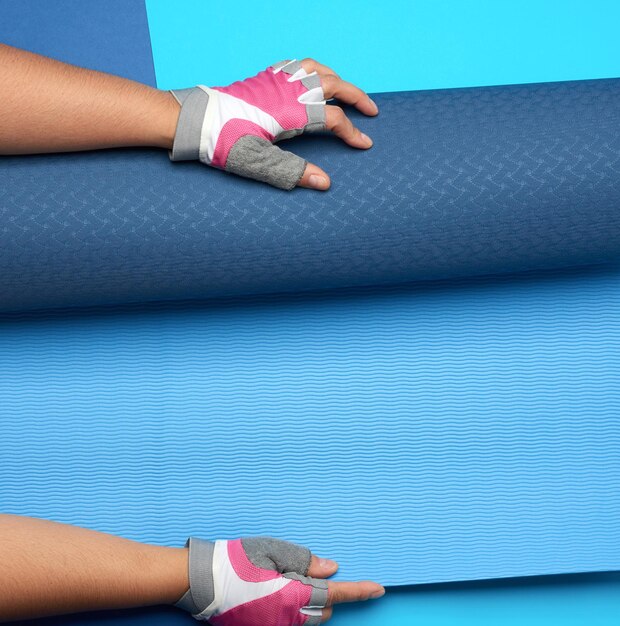 Female hand holds a rolled up neoprene sports mat on a blue background top view