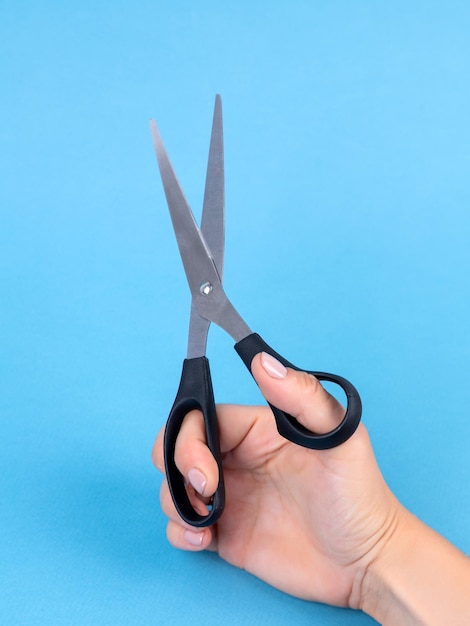 Female hand holds scissors on blue background