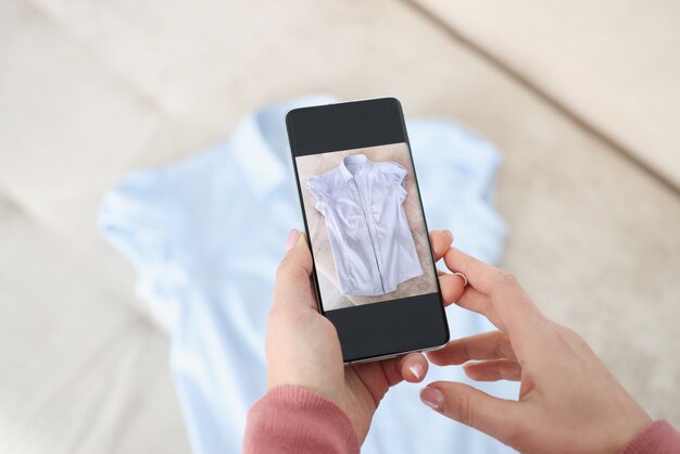 Female hand holds smartphone and makes photos of blue shirt