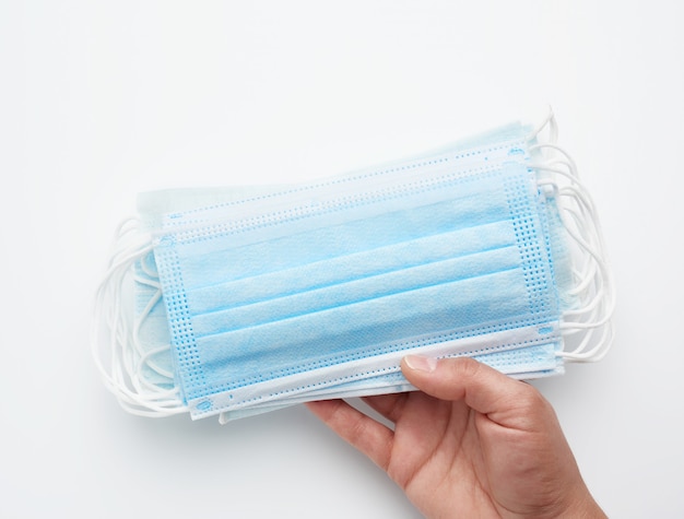 Female hand holds a stack of disposable medical face masks against viral diseases