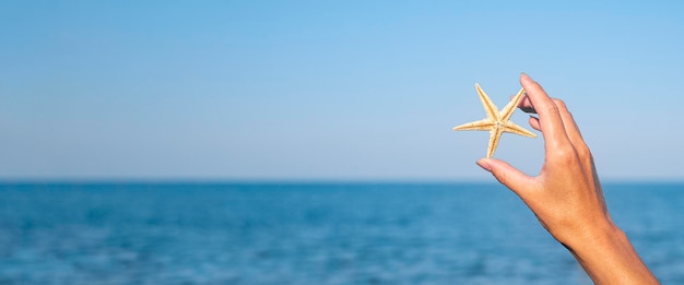 Female hand holds a starfish against the background of the sea sky Banner