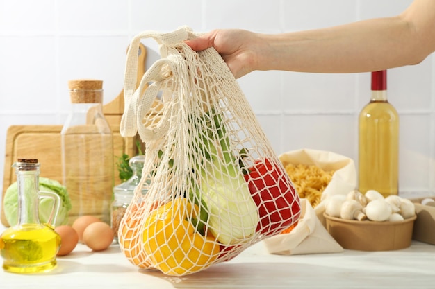 La mano femminile tiene la borsa di stringa con il concetto di cibo fresco di cottura