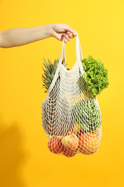 Female hand holds string bag with grocery on yellow
background