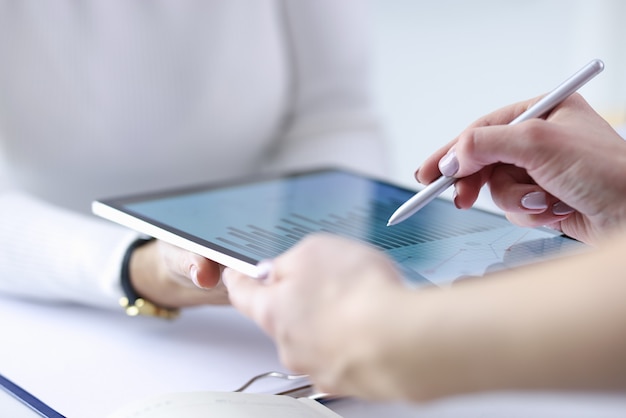 Photo female hand holds stylus over included tablet with business records together with colleague.