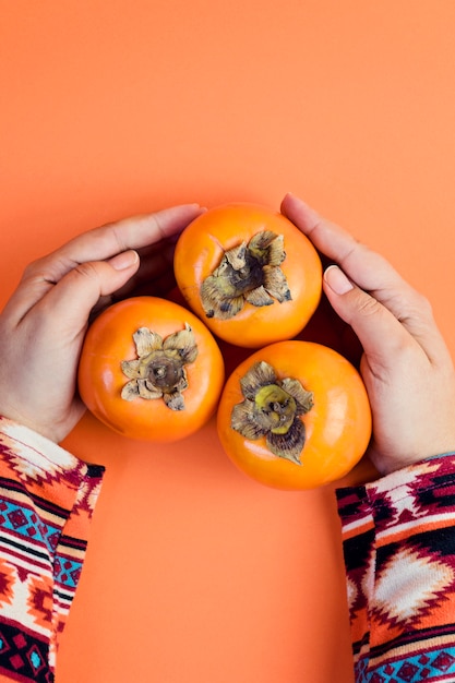 Female Hand holds three ripe persimmon on orange.