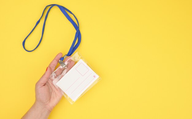 Female hand holds transparent plastic badge on a blue lanyard on a yellow background