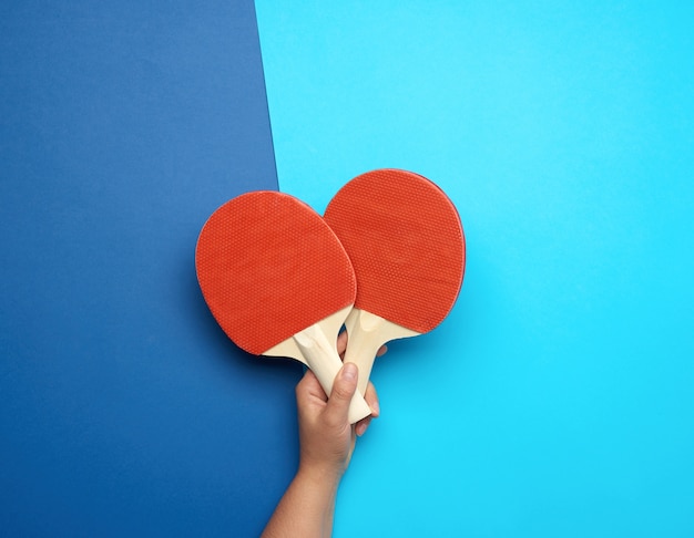 Female hand holds two wooden ping pong rackets on blue background