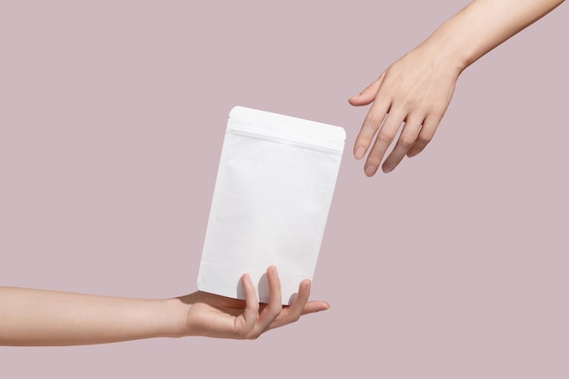 Female hand holds white cardboard packaging for tea coffee snack on pink background Mockup