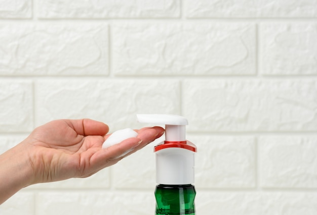 Female hand holds white foam squeezed out of a plastic dispenser, antiseptic, close up