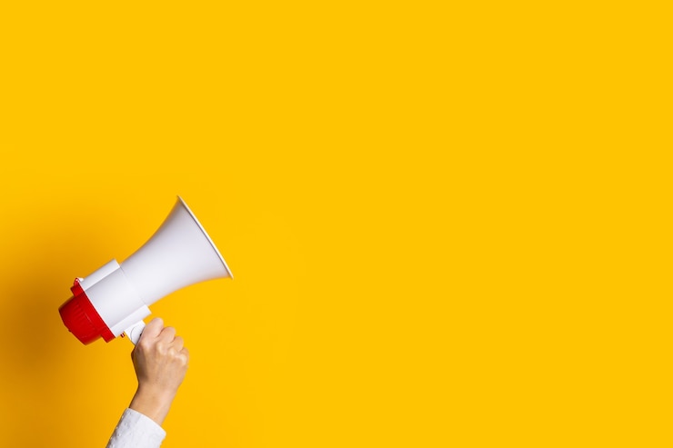 Photo female hand holds a white with a red megaphone on a yellow background