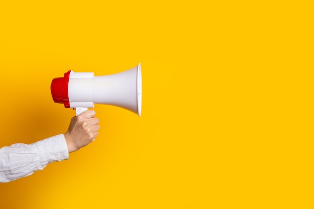 Female hand holds a white with a red megaphone on a yellow background