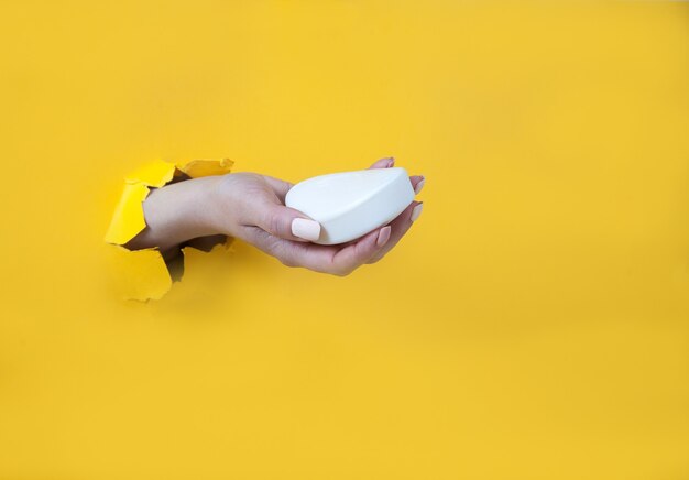 Female hand in a hole on yellow holds a white soap