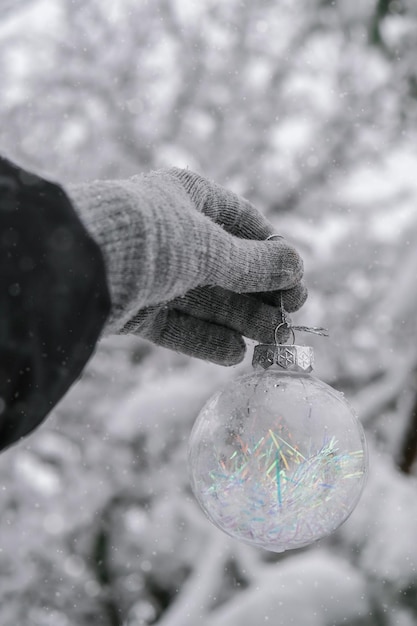 写真 冬の森の雪に覆われた枝もみの手袋透明なトレンディなガラス クリスマス ボールの女性の手