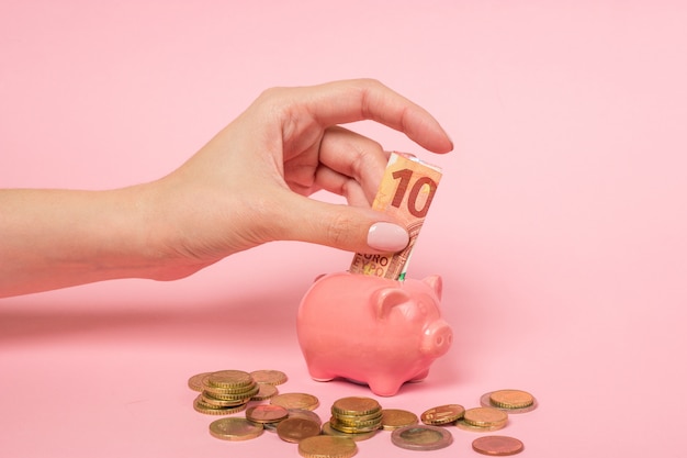 Female hand inserting a ten euro bill into a pink ceramic piggy bank