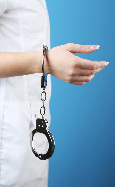 Female hand is handcuffed at wrist on blue background