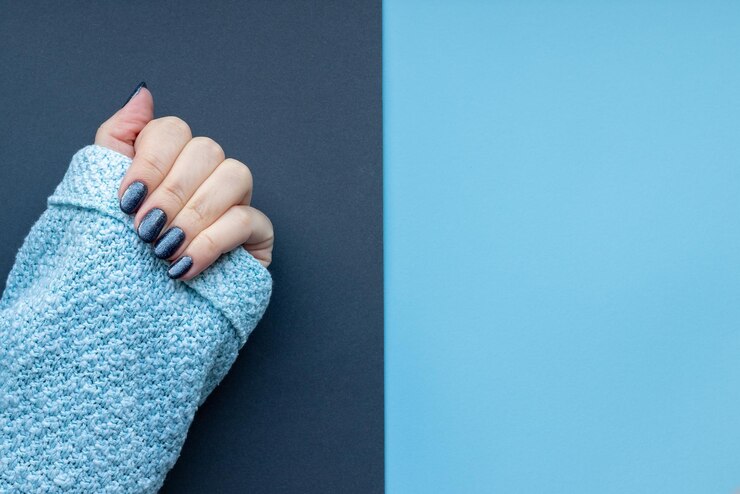 Female hand in knitted sweater fabric with beautiful manicure dark glittered nails on gray and blue