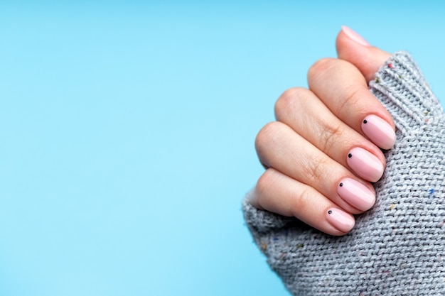 Female hand in knitted sweater with pink nude nails with black small dots on blue background