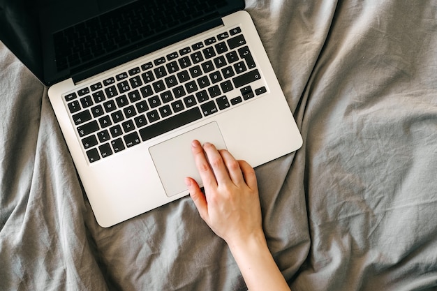 Female hand on laptop on bed.