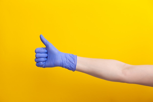 Female hand in lilac glove shows gesture thumb up or like