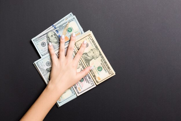 Female hand lying on stack of various dollar bills on colorful background. Saving money and wellbeing concept.