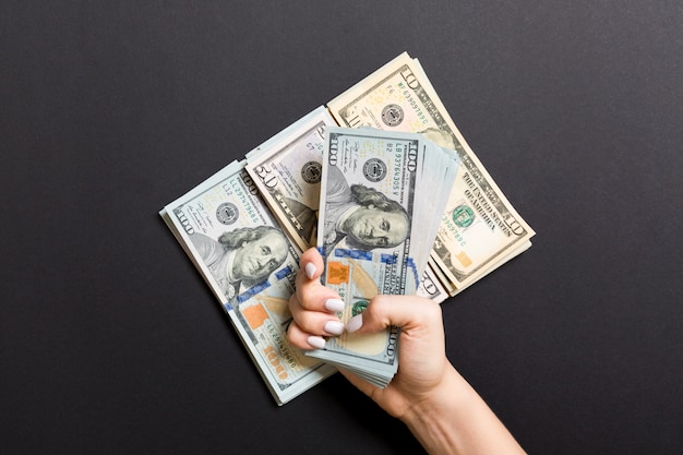 Female hand lying on stack of various dollar bills on colorful. Saving money and wellbeing concept