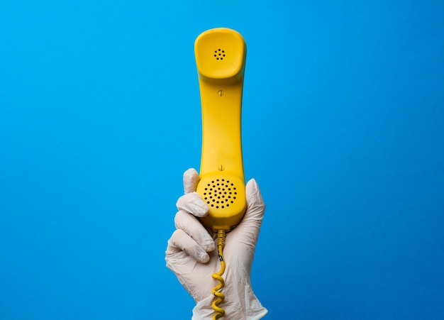 Female hand in medical glove holding yellow telephone speaker