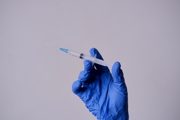 医療用手袋をかぶった女性の手は白い背景の薬に注射器を握っています