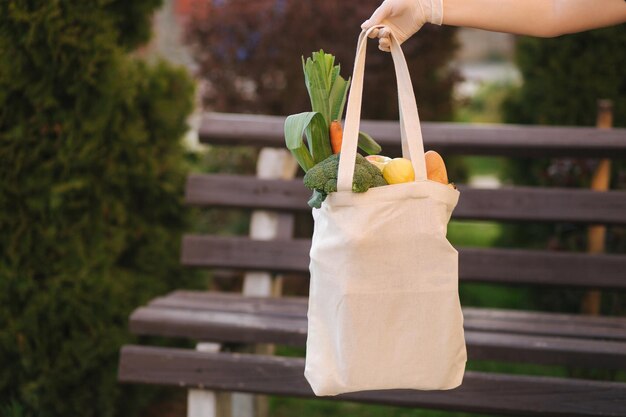 Photo female hand in medical gloves hold bag with fresh food vegetables fruits bread after shop in grocery