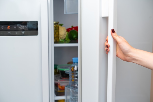 Female hand opens door of a fridge close up