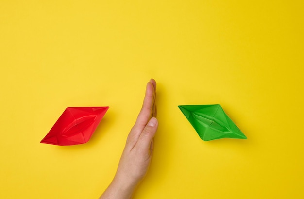 Female hand between paper boats on a yellow background the concept of reconciliation of the parties the search for compromises The role of the negotiator in the dialogue